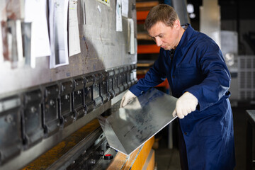 Focused professional craftsman in metalworking shop operating press brake, carefully positioning...