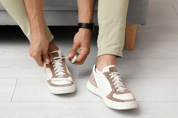 Stylish young man tying shoe laces at home, closeup