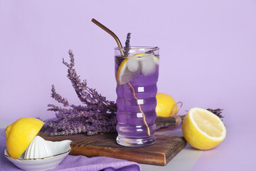 Wooden board with glass of lavender lemonade, flowers and lemons on color background