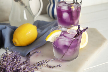 Board with glasses of cold lavender lemonade and lemons on light wooden table