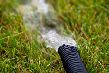 Residential sump pump drain line discharging water into grass yard after a rainstorm 