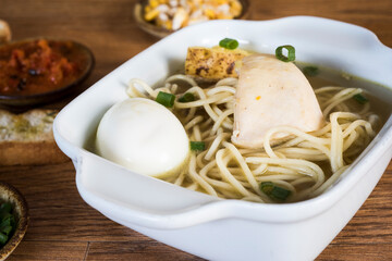 Typical Peruvian dish known as chicken soup, in a wooden bowl with lemon and chives.