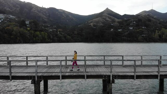 woman photographer in colorful clothes enjoys a walk on the Governors Bay Jetty, admiring beautiful coast near Lyttelton and Christchurch in Canterbury, New Zealand South Siland