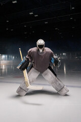 Dark silhouette of a male hockey player in a uniform, helmet and skates with a stick on the ice arena with smoke and blue back light