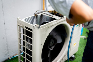 An air conditioner technician's hand holds a high pressure water hose to clean the air conditioner compressor.