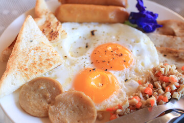 Breakfast with fried eggs, bacon, sausages and toast bread on wooden table outdoor in resort. Healthy food. 