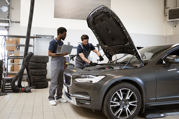 Mechanics working on car maintenance in modern auto repair shop, using laptop and tools. Auto repair, service check, and team collaboration displayed.