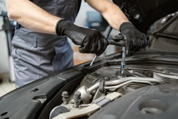 Mechanic wearing gloves using wrench to fix car engine in auto repair shop. Focus on hands and tools demonstrating professional car maintenance.