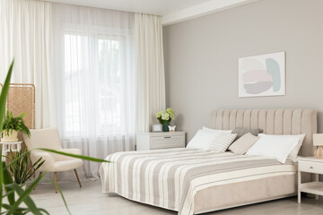 Large bed, nightstand, chest of drawers, armchair and window with curtains in bedroom. Interior...