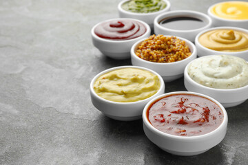 Many different sauces in bowls on grey table, closeup. Space for text