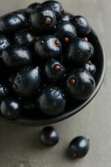 Ripe black currants in bowl on grey table, closeup
