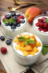 Tasty yogurt with fresh berries, fruits and mint in glasses on table, closeup