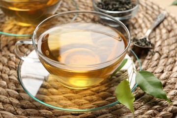 Refreshing green tea in cup and leaves on wicker mat, closeup