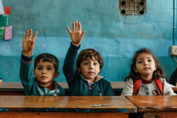 Three primary school students in the classroom with raised hands, eagerly waiting to answer the teacher’s questions, showcasing an engaged learning environment and enthusiasm for education.