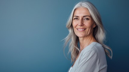 Middle-aged woman in a half-body shot, smiling warmly with a solid blue background, providing clear copy space on the left