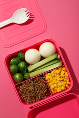 Pink lunch box with healthy food on a pink background