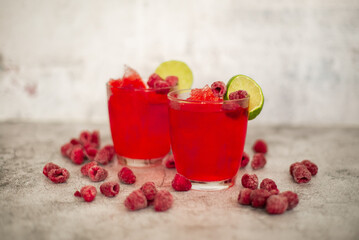Summer cocktail with raspberry puree and crushed ice, decorated we itch raspberries and lemon, concrete background with natural raspberries.