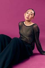 Fashion asian woman in sheer top and black pants sitting on purple background with eyes closed and...