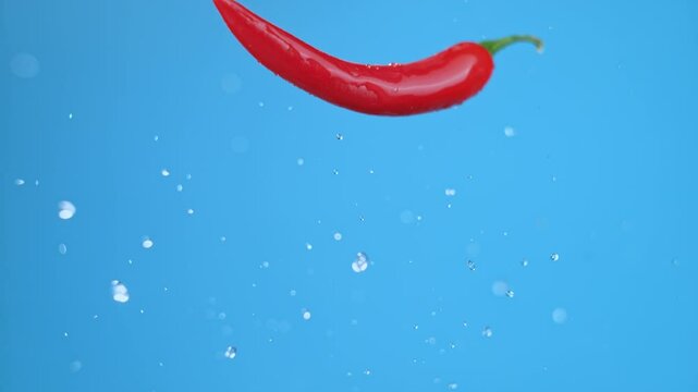 Single large red chili bell pepper flying into the frame and flipping once with water droplets. High quality cinematic studio commercial super slow motion 1000fps fresh pepper moving up and down.