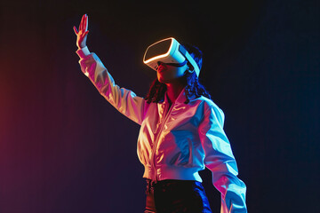 Excited young woman touching air while having virtual reality experience in neon light
