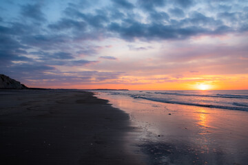 Serene beach scene at sunrise, colorful sky, reflections on wet sand, peaceful and tranquil atmosphere