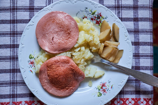 Traditional meal with mashed potatoes, fried bologna sausage (parizer), and pickles on a floral plate
