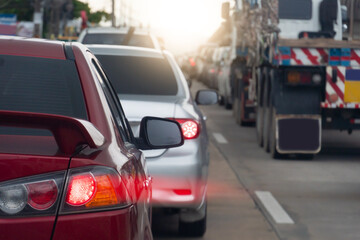 Rear side of red car on the road. Concrete road with many car during time on traffic jam. Speed light lines on the tail lights. Car parked in a long queue.