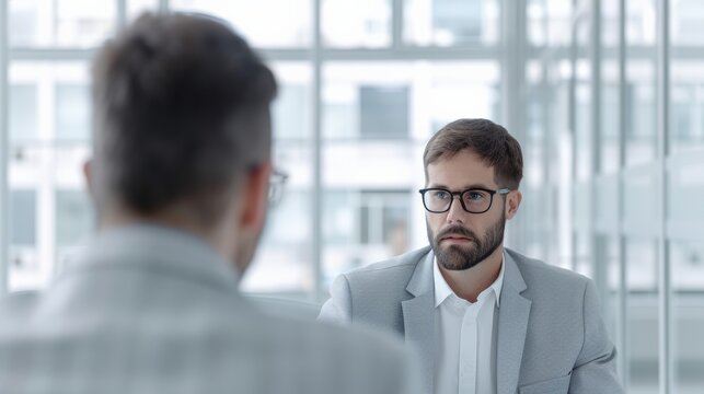 Professional business meeting with serious discussion between two men in modern office setting, both in formal attire.
