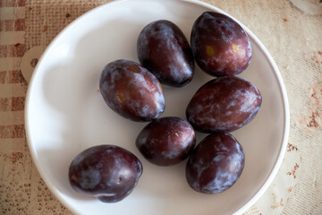 Fresh plums on a white plate with a rustic tablecloth background