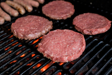 Raw minced meat for home made grill burgers cooking with spaces and herbs.bbq.some fresh and juicy hamburgers cooking on the grill. and sausages Cooking Over Flames On The Grill.