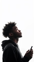 A young man in a hoodie looks up thoughtfully against a white background, holding an object in his hand