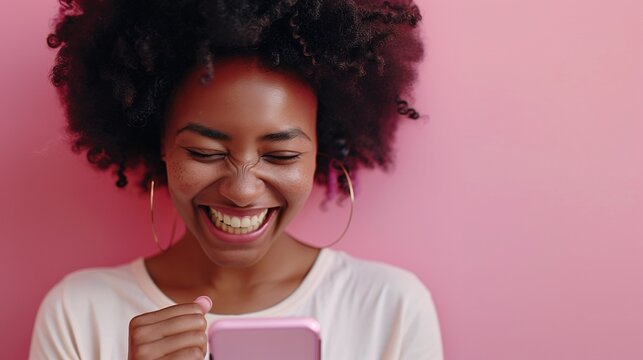 Excited African American woman celebrating a victory on her smartphone, web app and mobile app: betting, games, cryptocurrency exchanges, rewards, and social fun, solid pink color.