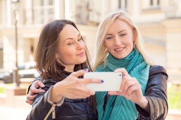 Two girl friends take a selfie portrait on a smartphone. Young women walk around the city and take pictures on their phones.