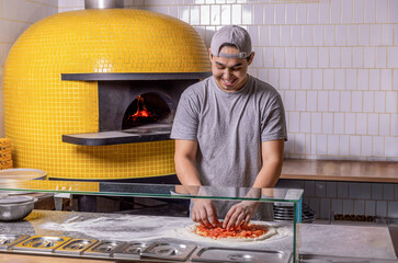 Cook hand makes a pizza, puts the sausage on top. Hand sprinkling cheese on pizza dough with tomato...