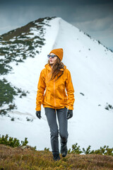 Woman hiker hiking in snowy mountain area wearing cold weather accessories, wind jacket and...