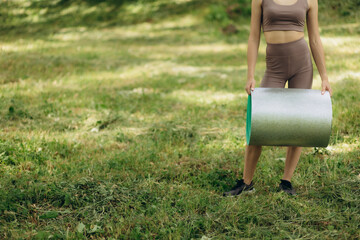 Athletic young woman in sportswear in park rolls up yoga mat.