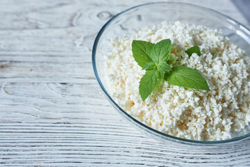 Cottage cheese with mint in glass bowl on wooden table, closeup