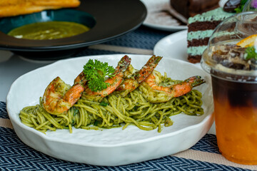 Green spaghetti with shrimp on top and has food and drinks