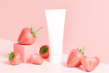 Single white empty facial cosmetic tube on pink theme geometric background decorated with strawberry for product mockup presentation