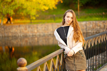 A young smiling girl walking in an autumn park in a good mood. Teenage girl, portrait against a background of nature. Fashion style trend.