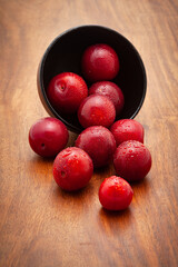 Front view of fresh Cherry Plum (Prunus cerasifera) fruits spilled out from a black ceramic bowl on a white background.
