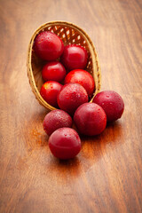 Top view of fresh Cherry Plum (Prunus cerasifera) fruits spilled out from a wooden basket, on a wooden background.