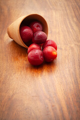 Front view of fresh Cherry Plum (Prunus cerasifera) fruits spilled out from a mud pot, on a wooden background.