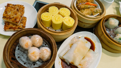 An arrangement of dimsum platters at a restaurant with rolled egg, shumai, rice noodle roll, and more, a classic cantonese lunch. 