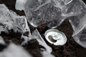 A photo depicting plastic bags, a plastic bottle, and aluminum cans buried in soil, highlighting...