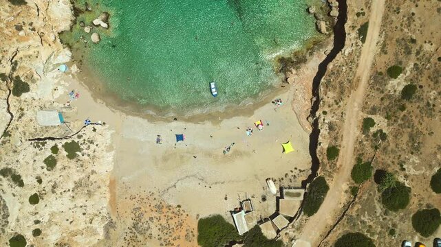 A pristine beach on the Greek island of Donousa, Cyclades, with turquoise waters lapping at the golden sand. People relax under colorful umbrellas, enjoying the summer sun.