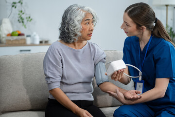 Fototapeta premium Female doctor checking old woman blood pressure at clinic and filling patient history in the morning.