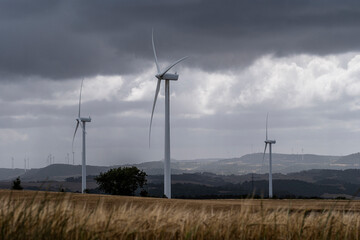 Three wind turbines stand tall in a vast field, captured under a dark and stormy sky, highlighting the contrast between nature's raw power and human technological innovation in Lerida Spain