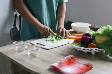 Man making salad, cut the lettuce leaves and put it into a bowl at the kitchen