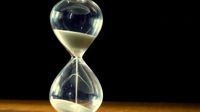 Closeup of time sand timer clock with sand flowing from through hourglass on black background. Fantasy art concept